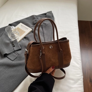 Detail of a brown suede bucket bag with leather paneling and silver round metal clasp
