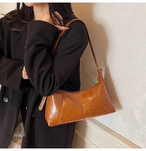 Brown oil wax leather baguette bag worn over the shoulder with black blazer jacket