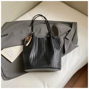 Detail view of black woven tote bag with bohemian bead charm and premium leather texture