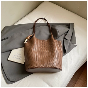 Close-up of brown hand-woven tote bag with leather straps and decorative bead charm
