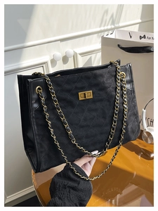 Close-up of black quilted suede tote bag with gold metal clasp and chain strap