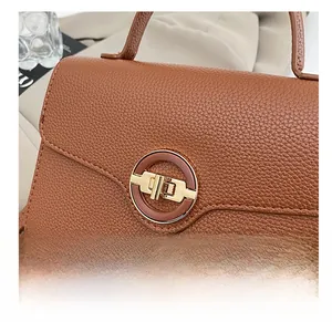 Détail de la texture cuir litchi marron et du fermoir rotatif en métal doré sur le sac à main