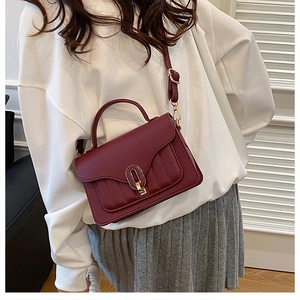 Close-up of burgundy lychee grain leather handbag with elegant gold oval metal buckle detail