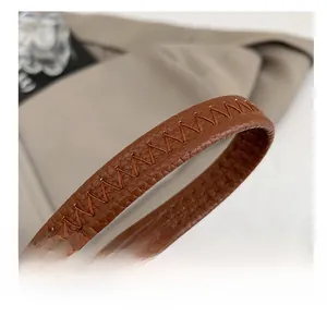 Gros plan d'une bandoulière en cuir grainé marron avec surpiqûres en Z décoratives