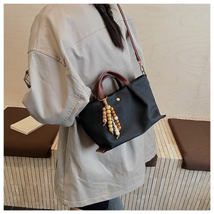 Detail of minimalist black crossbody bag with wooden bead tassel and leather handle