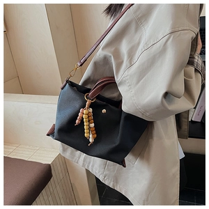 Detail of black canvas crossbody bag with wooden bead tassel and magnetic buckle