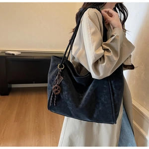 Detail view of black suede tote bag with brown pendant worn by a model for daily commute