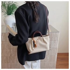 Detail of a cream canvas crossbody bag with wood bead tassel shown on a model