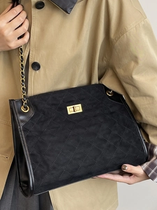 Vintage black quilted suede tote bag with gold hardware and chain strap on a trench coat
