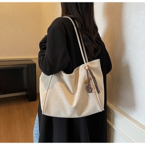 Minimalist beige tote bag with litchi texture and ribbon charm worn on shoulder