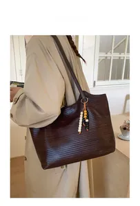 Sac fourre-tout tressé marron foncé avec pendentif perlé porté de côté sur un trench beige