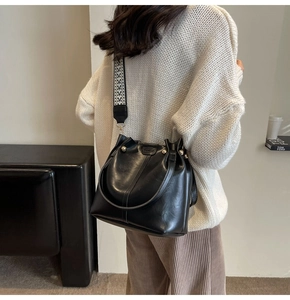 Detail of black PU leather bucket bag with wide geometric strap and golden hardware