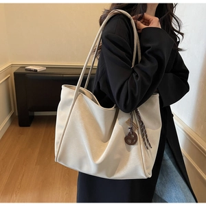 Detail view of cream tote bag featuring brown circular charm and woven leather texture