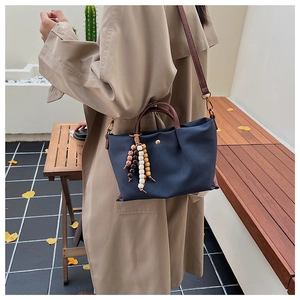 Detail of navy canvas bag with brown leather strap and wooden bead charm accessory