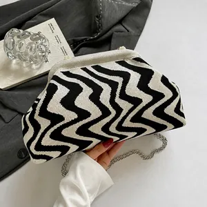 Macro detail of wave-patterned knit fabric and silver chain on minimalist pouch bag