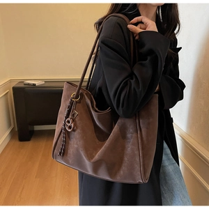 Detailed view of brown suede tote bag featuring braided knot detail and golden buckle