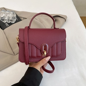 Detail view of burgundy lychee leather bag with elegant oval metal lock and handle