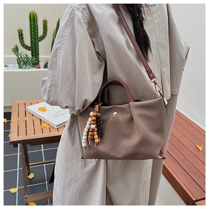 Detail of dark brown canvas crossbody bag with wooden bead tassel and leather strap
