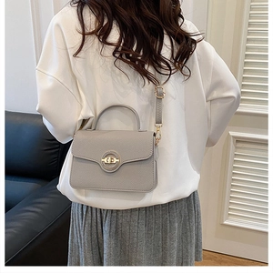 Détail du sac à main en cuir gris avec fermoir doré circulaire porté par un mannequin