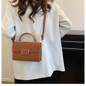 Detailed view of a brown pebbled leather crossbody bag with a gold square clasp on a model