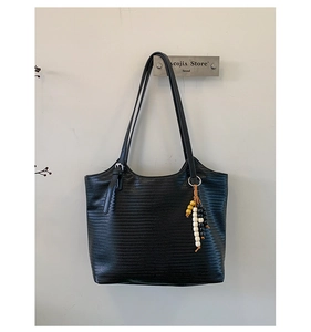 Détail du sac cabas tissé noir avec un pendentif en perles décoratif et fines bandoulières
