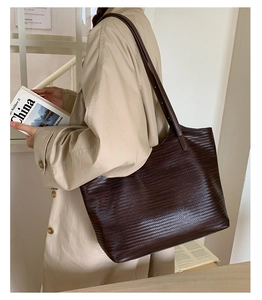 Détail du grand cabas en cuir tressé marron foncé porté avec un trench beige