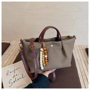 Detail of canvas bag with leather strap and wooden bead accessory on a wooden table