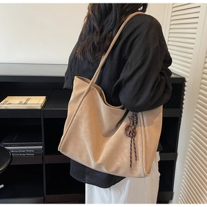 Detailed close-up of a large beige tote bag with a brown woven knot pendant accessory