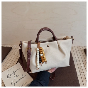 Detail of canvas tote bag with brown leather handles, pleated sides and wooden beads charm