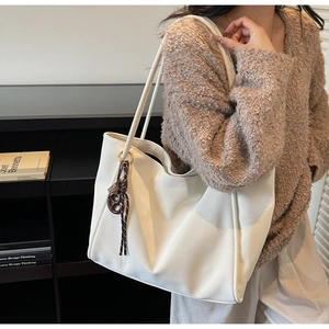 Close-up of white tote bag with soft leather texture and brown knotted pendant detail
