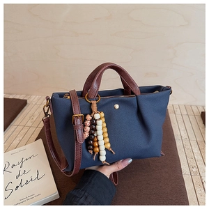 Detail of navy canvas crossbody bag with brown leather handle and colorful beaded charm