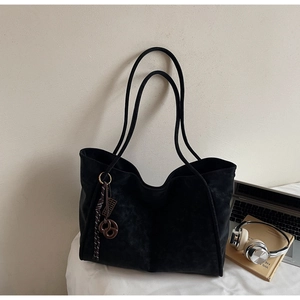 Macro shot of black suede tote bag with woven knot charm on an office desk setting