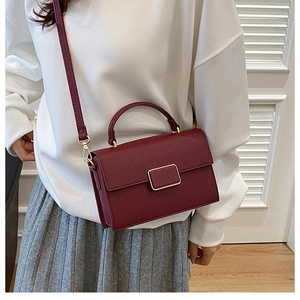 Detail of burgundy lychee grain leather handbag with gold buckle and crossbody strap