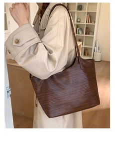 Gros plan d'un grand sac cabas tissé marron foncé porté avec un trench-coat beige