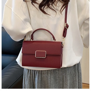 Detail of dark red pebble leather crossbody bag with gold buckle on a model outfit