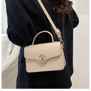 Sac à bandoulière chic en cuir beige avec fermoir doré sur un blazer noir élégant