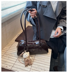 Detail of dark brown glossy Boston bag with gold logo and cute bear charm pendant
