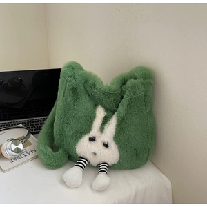 Detail of green plush bunny crossbody bag on a desk with laptop and headphones