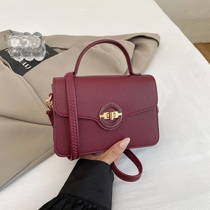 Détail d'un sac à main en cuir grainé bordeaux avec un fermoir rotatif en métal doré