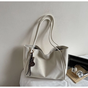 Detail of minimalist cream tote bag showing soft leather texture and stylish charm accessory