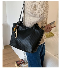 Détail du sac cabas tissé noir avec fine bandoulière et pendentif en bois perlé