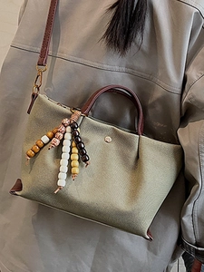 Olive green canvas crossbody bag with brown leather straps and ethnic beaded pendant