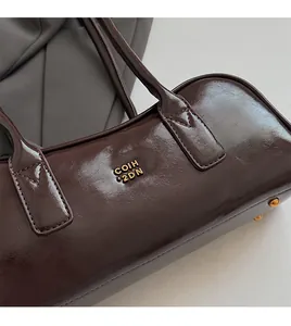 Close-up of dark brown glossy Boston bag with gold logo lettering and metal bottom feet