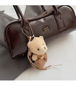 Close-up of a plush bear charm in beige sherpa with striped overalls on a brown bag