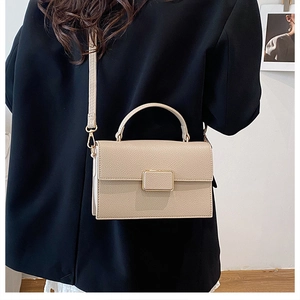 Detail of beige lychee pattern crossbody bag with gold metal buckle on female model