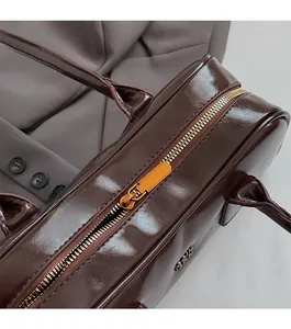 Close-up of golden zipper and glossy dark brown patent leather on Boston bag