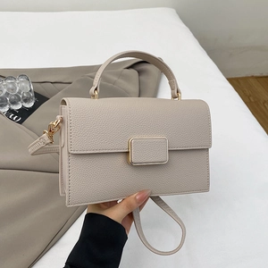 Detail of a beige pebbled leather handbag with a golden clasp and top handle