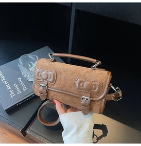 Detailed close-up of brown suede pillow bag with dual bow leather buckles and handle