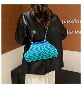 Model wearing a blue and green wave pattern knit crossbody bag with silver chain strap