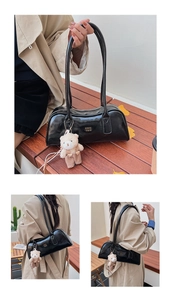 Detail of glossy black Boston bag featuring gold COIN lettering and a cute plush bear charm